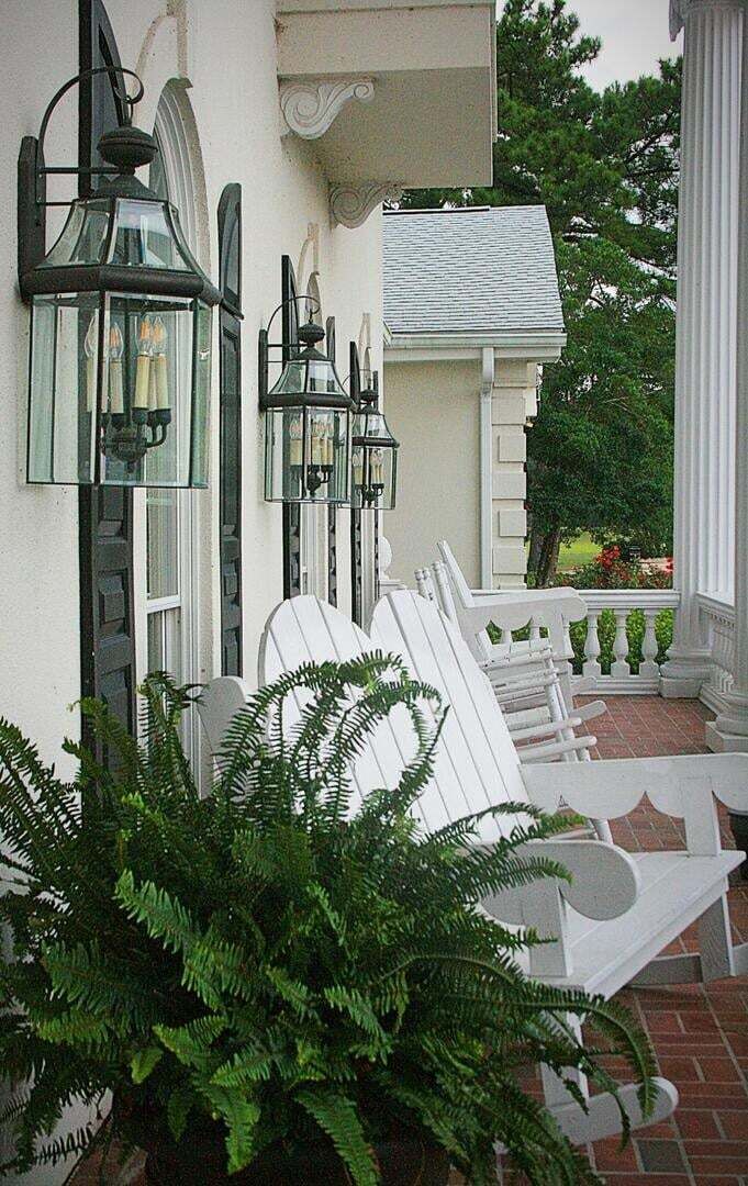 A porch with white chairs and a potted fern.