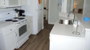 Uma cozinha com eletrodomésticos brancos, uma pia de aço inoxidável e piso de madeira.