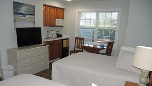 Quarto de hotel com duas camas, televisão, cozinha compacta e janela com persianas.