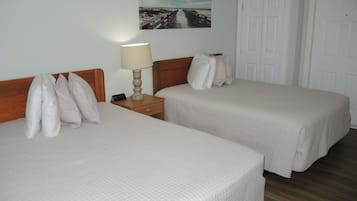 Two single beds with white bedding, a bedside table with a lamp, and a painting on the wall.