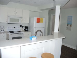 Una cocina moderna con armarios blancos, microondas, estufa, refrigerador y cafetera.