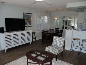 Sala de estar con televisor, comedor, cocina y ventilador de techo.