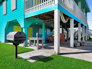 Ein türkisanes Gebäude mit Veranda, Grill und gelber Tür.