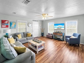 A living room with a grey sofa, a blue armchair, a coffee table, and a TV on the wall.
