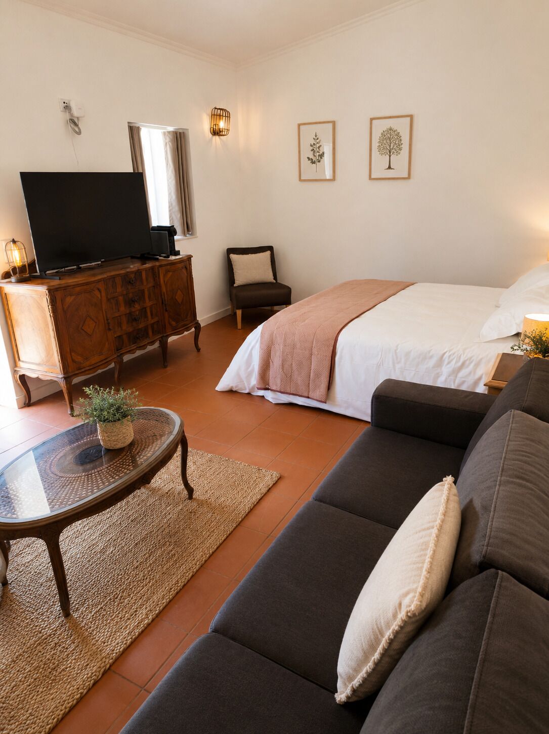 Een moderne woonkamer met een flatscreen televisie, een bank, een salontafel met een plant en een bed met een witte dekbedovertrek.