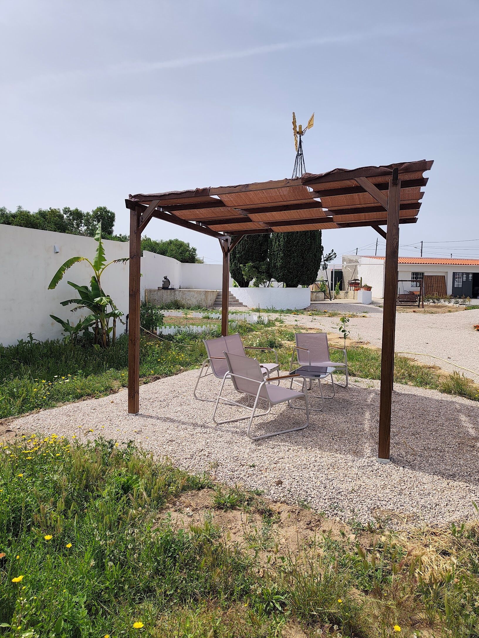 Un espacio al aire libre con techo, dos sillas, una pérgola y suelo de grava.