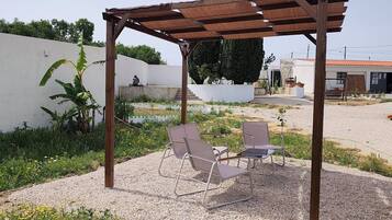 Un espacio al aire libre con techo, dos sillas, una pérgola y suelo de grava.