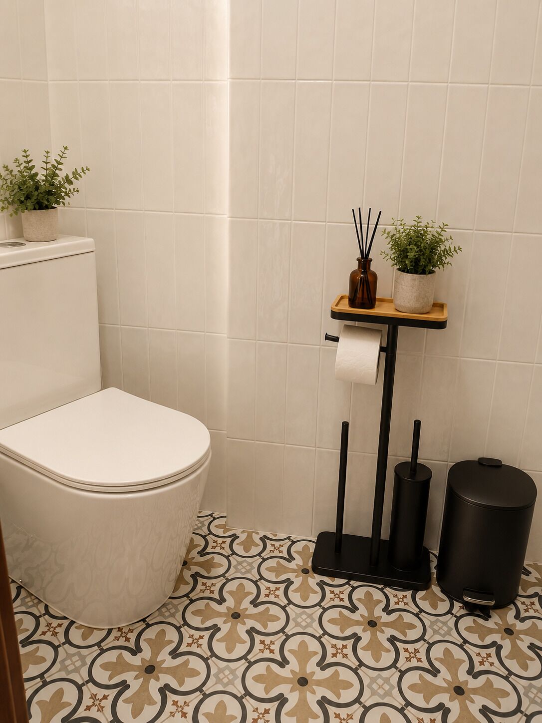 Un baño con inodoro, soporte para papel higiénico, un cubo de basura y dos plantas en macetas sobre una estantería.