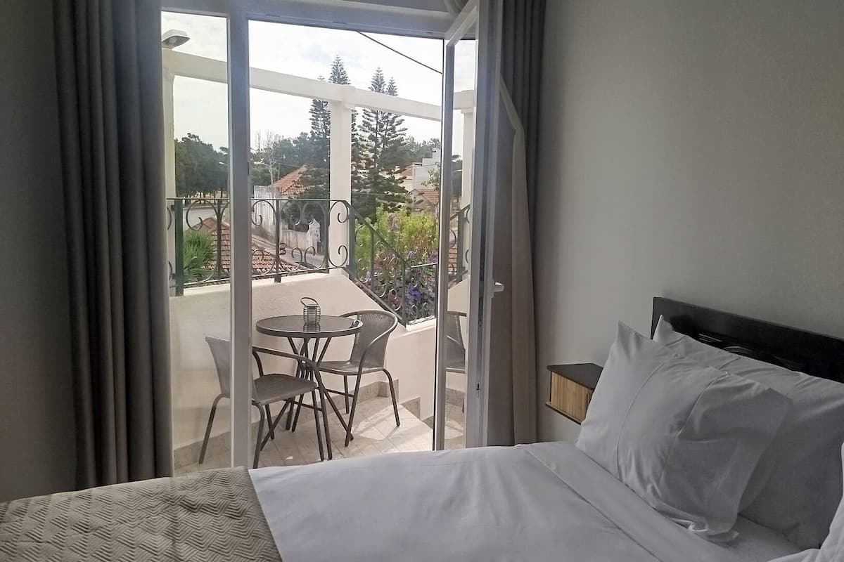 A hotel room with a bed, a balcony with a table and chairs, and a view of the surrounding area.