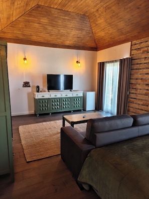Una sala de estar con techo de madera, un aparador verde, un televisor de pantalla plana, un sofá y una ventana con cortinas.