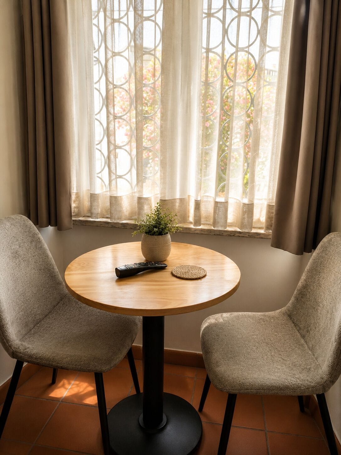 Una mesa redonda de madera con dos sillas, un control remoto y una planta pequeña.