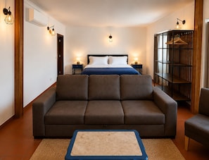A hotel room with a bed, a sofa, a small table, and a bookshelf.