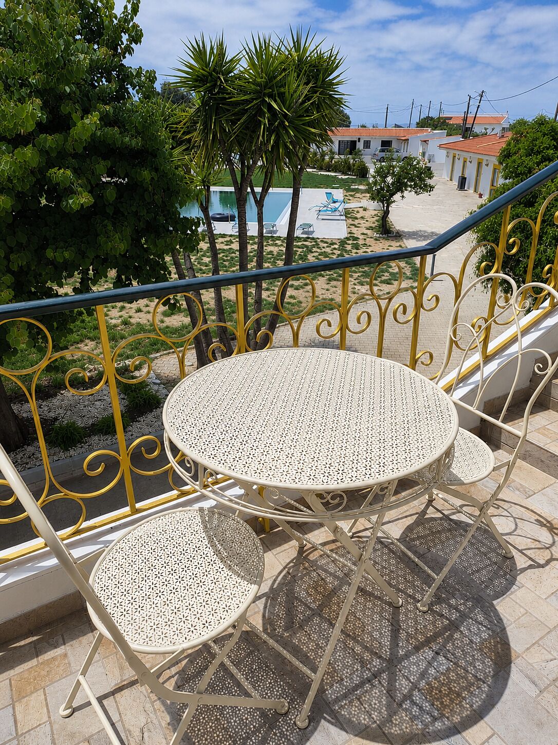 A balcony with a round table and two chairs, overlooking a swimming pool and a residential area.
