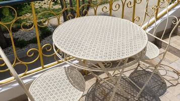 A balcony with a round table and two chairs, overlooking a swimming pool and a residential area.