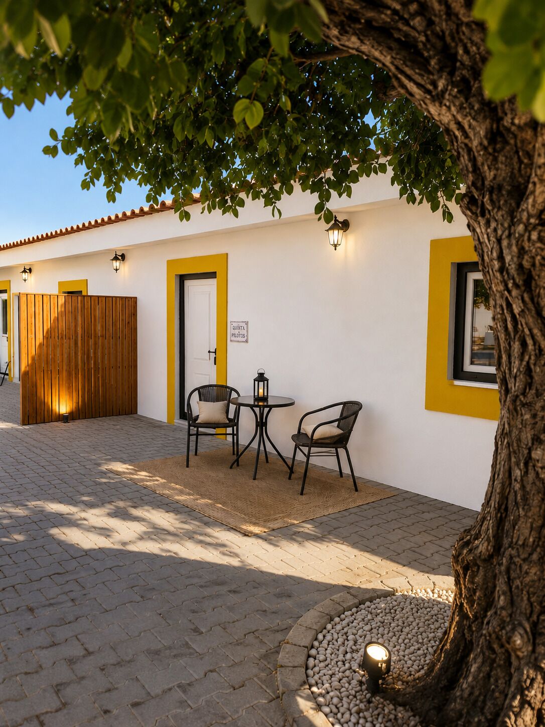 A courtyard with a wooden fence, a door labeled 'QUINTA PLOTS,' and two tables with chairs.
