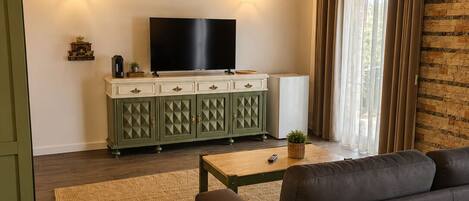 Una sala de estar con una televisión de pantalla plana, un mueble verde, un sofá y una mesita de centro.