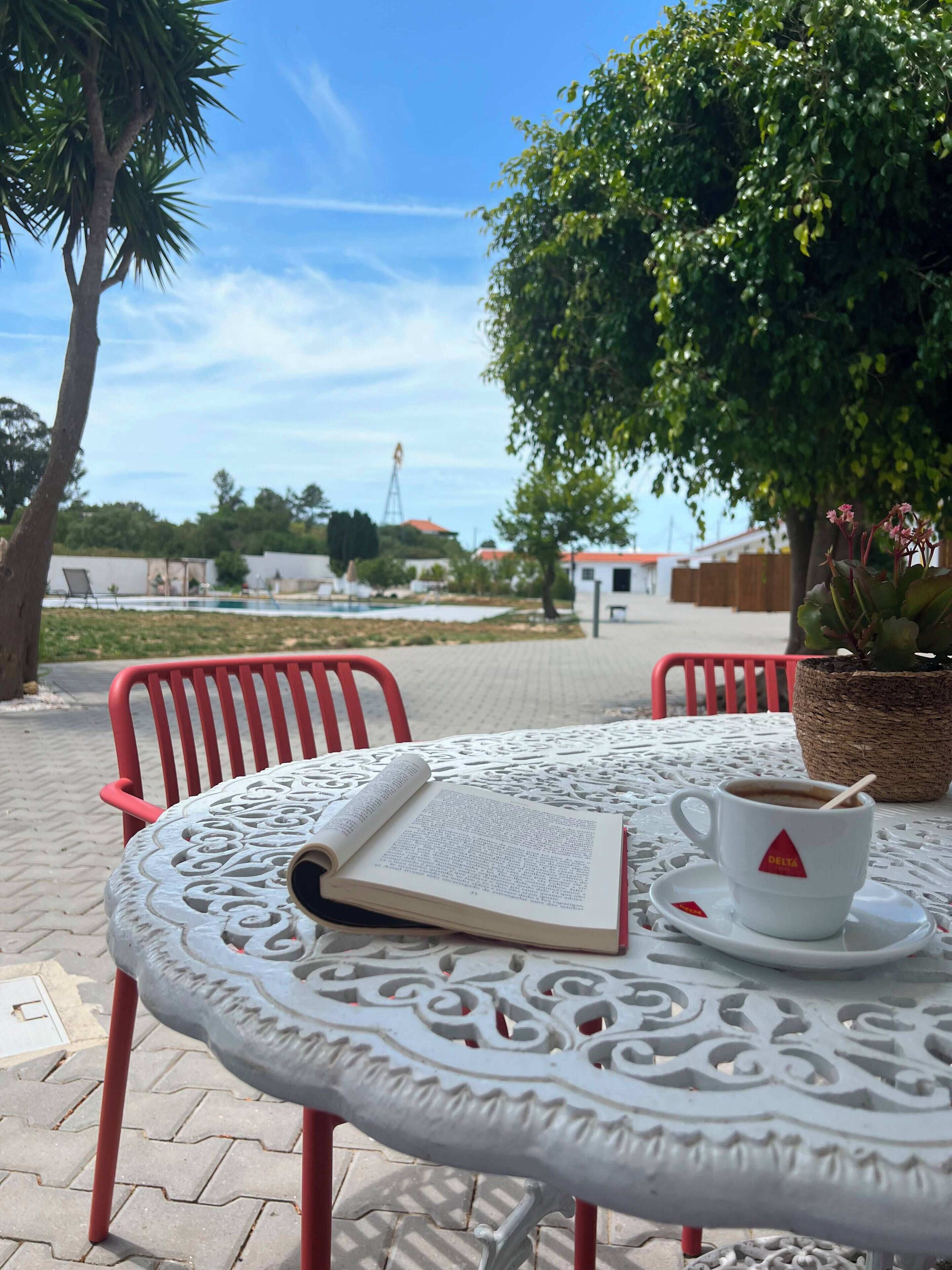 A round outdoor table with a white tablecloth, a book, a cup of coffee, and a potted plant.