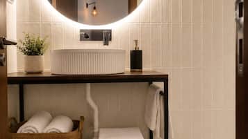 A bathroom with a round mirror, white sink, towel rack, and a woven basket.