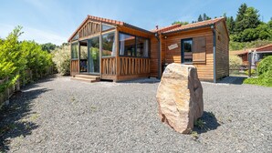 A wooden cabin with a glass porch, a stone centerpiece, and a gravel driveway. - Chalet l'Entékia near Gérardmer with Billiards and Private Spa (Corcieux)