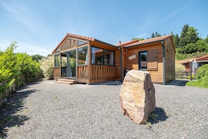 Eine Holzhütte mit einer Glasveranda, einem Steintisch und einer Schotterauffahrt.
