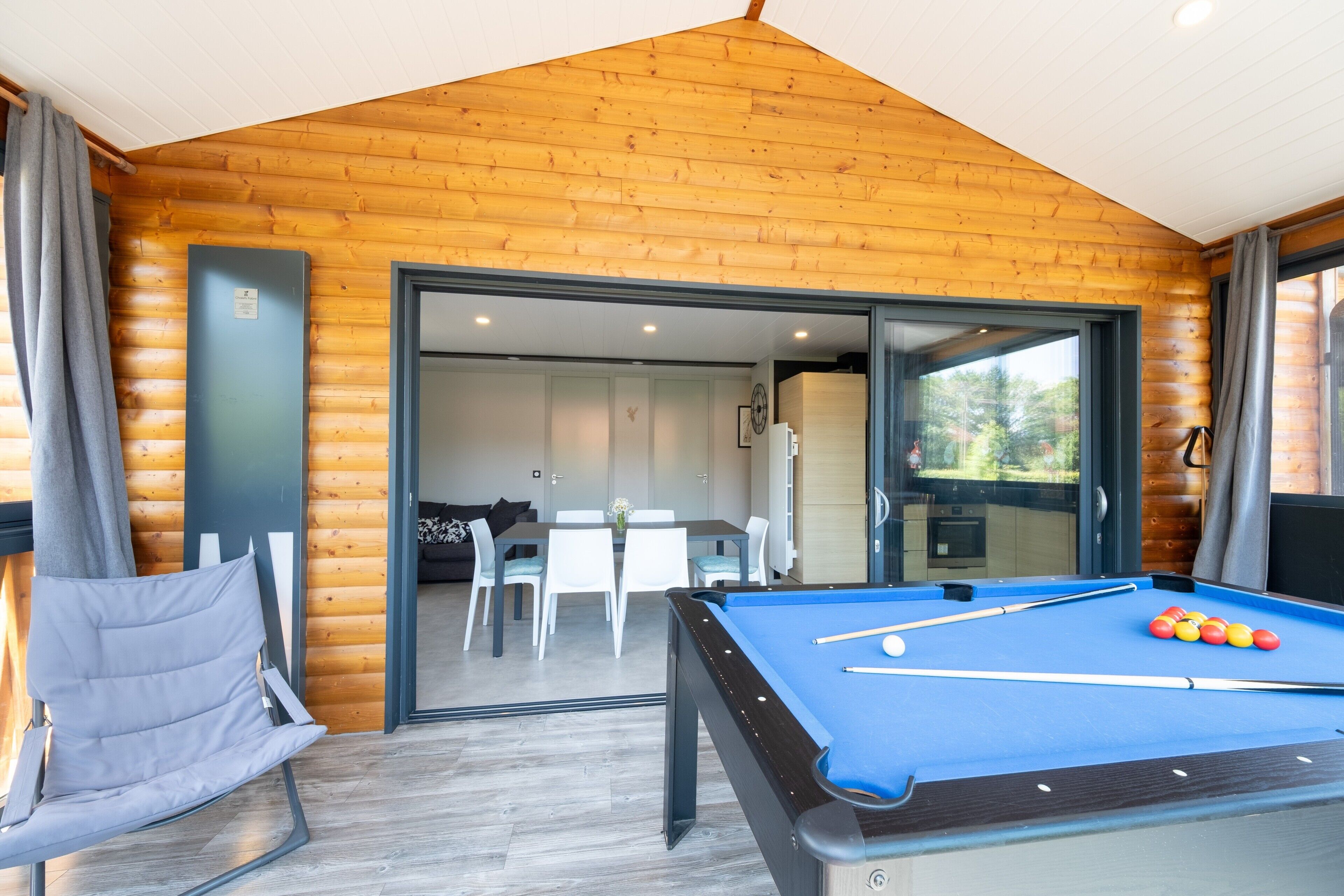 A pool table in a room with wooden walls and a dining area visible through a glass door.