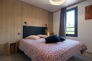 Ein modernes Schlafzimmer mit einem großen Bett, einem Nachttisch, einer Wandlampe und einem Fenster mit Vorhängen.