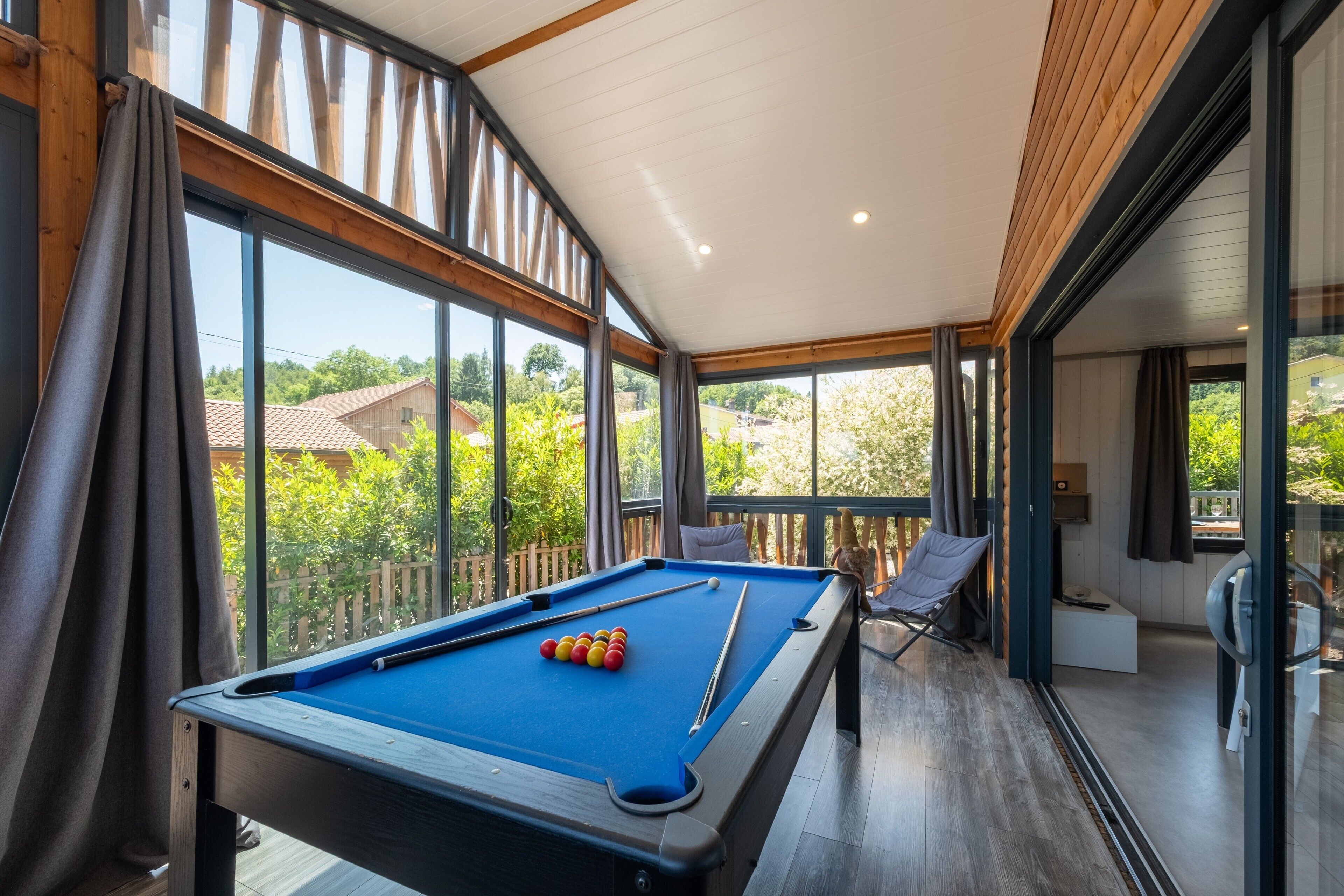 A pool table in a room with large windows, a chair, and a bench.