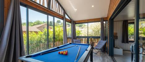 A pool table in a room with large windows, a chair, and a bench.