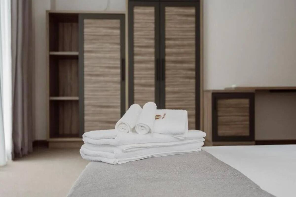 A neatly arranged stack of white towels on a bed in a hotel room with a wooden wardrobe and a small table.