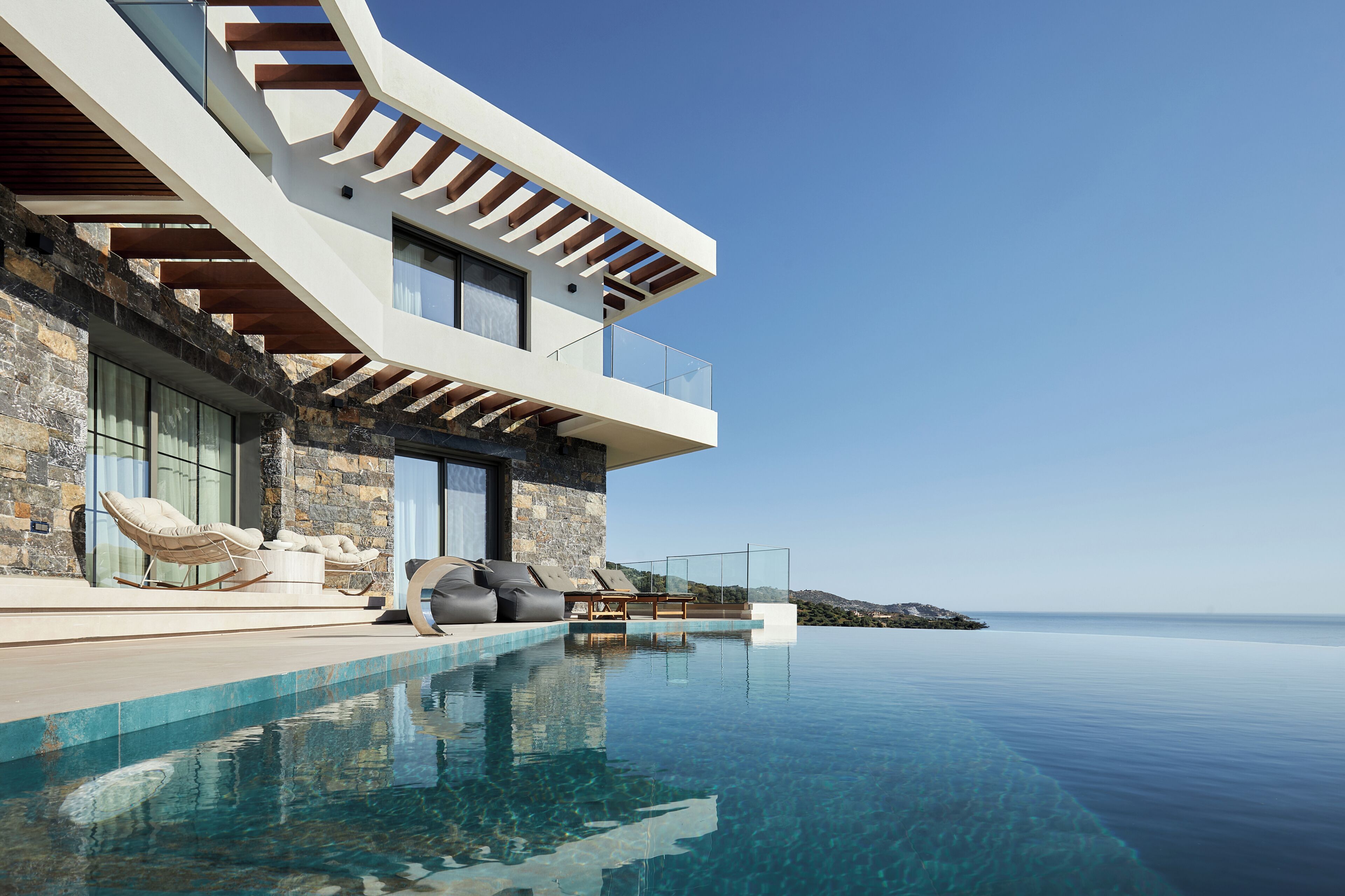 A modern house with a pool, stone facade, and a clear view of the sea.