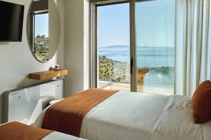 A bedroom with a bed, a TV, a heater, a window with a view of the sea, and a balcony. - Villa Gaia Sea Horizon (Rodia Heraklion)