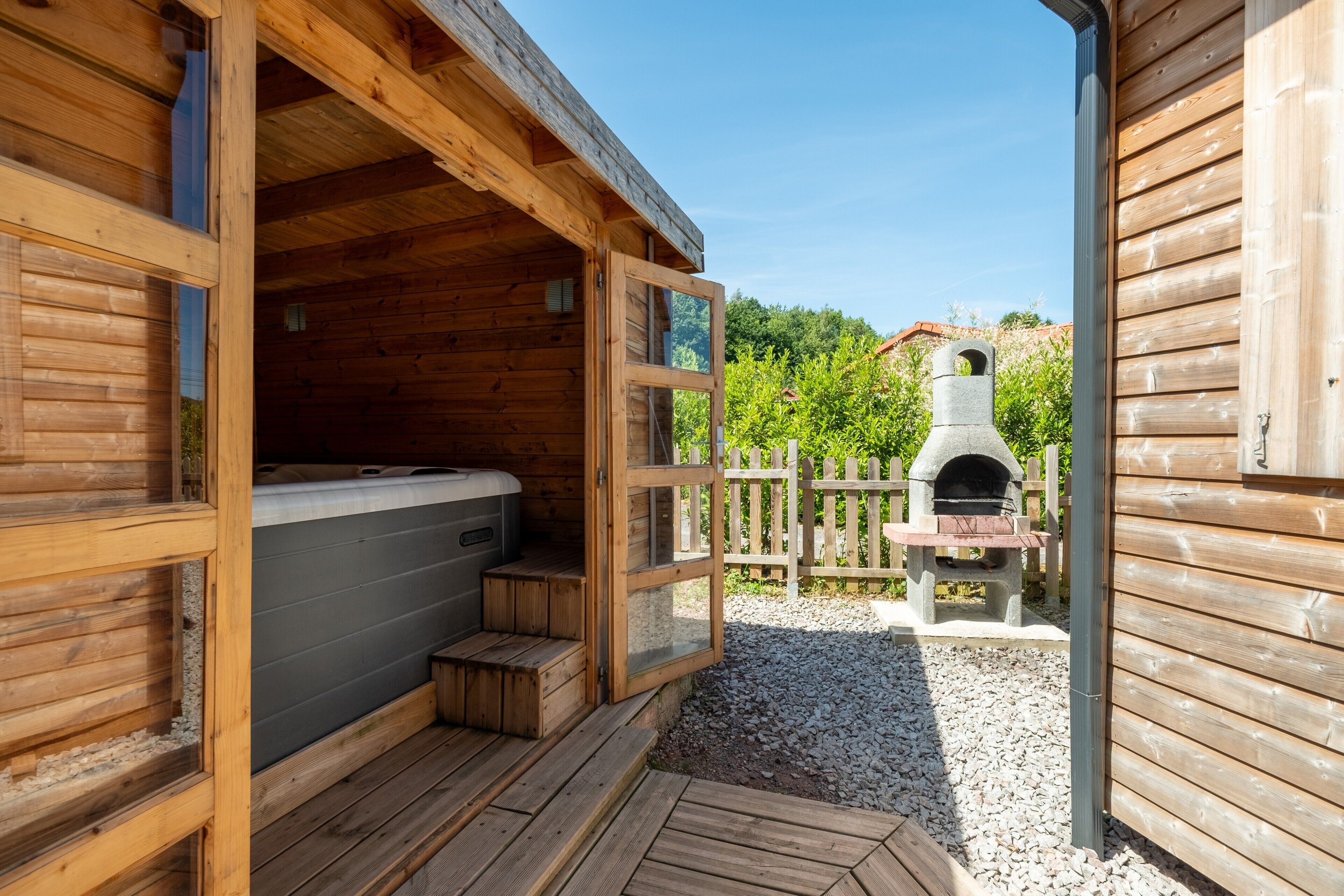 A wooden cabin with a hot tub, a stone fireplace, and a gravel patio.