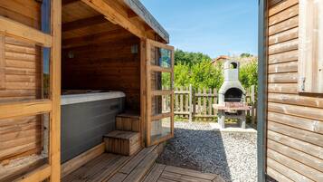 A wooden cabin with a hot tub, a stone fireplace, and a gravel patio.