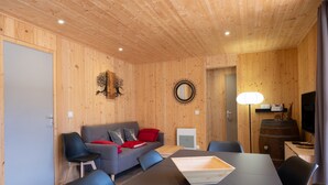 Um quarto com painéis de madeira, incluindo um sofá, cadeiras, uma mesa, um abajur e uma televisão.