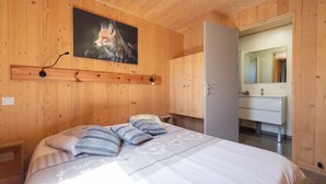 Quarto com painéis de madeira, uma cama, um quadro de uma raposa e um banheiro com espelho.