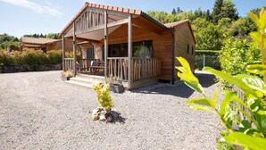 Une cabane en bois à deux étages, dotée d’un balcon et entourée de gravier et de verdure.