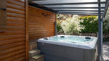 Un bain à remous dans un chalet en bois, surmonté d’une pergola.