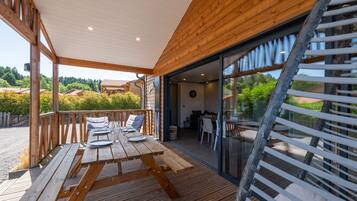 Une terrasse en bois avec une table dressée pour le repas, un escalier et une vue sur le paysage environnant.