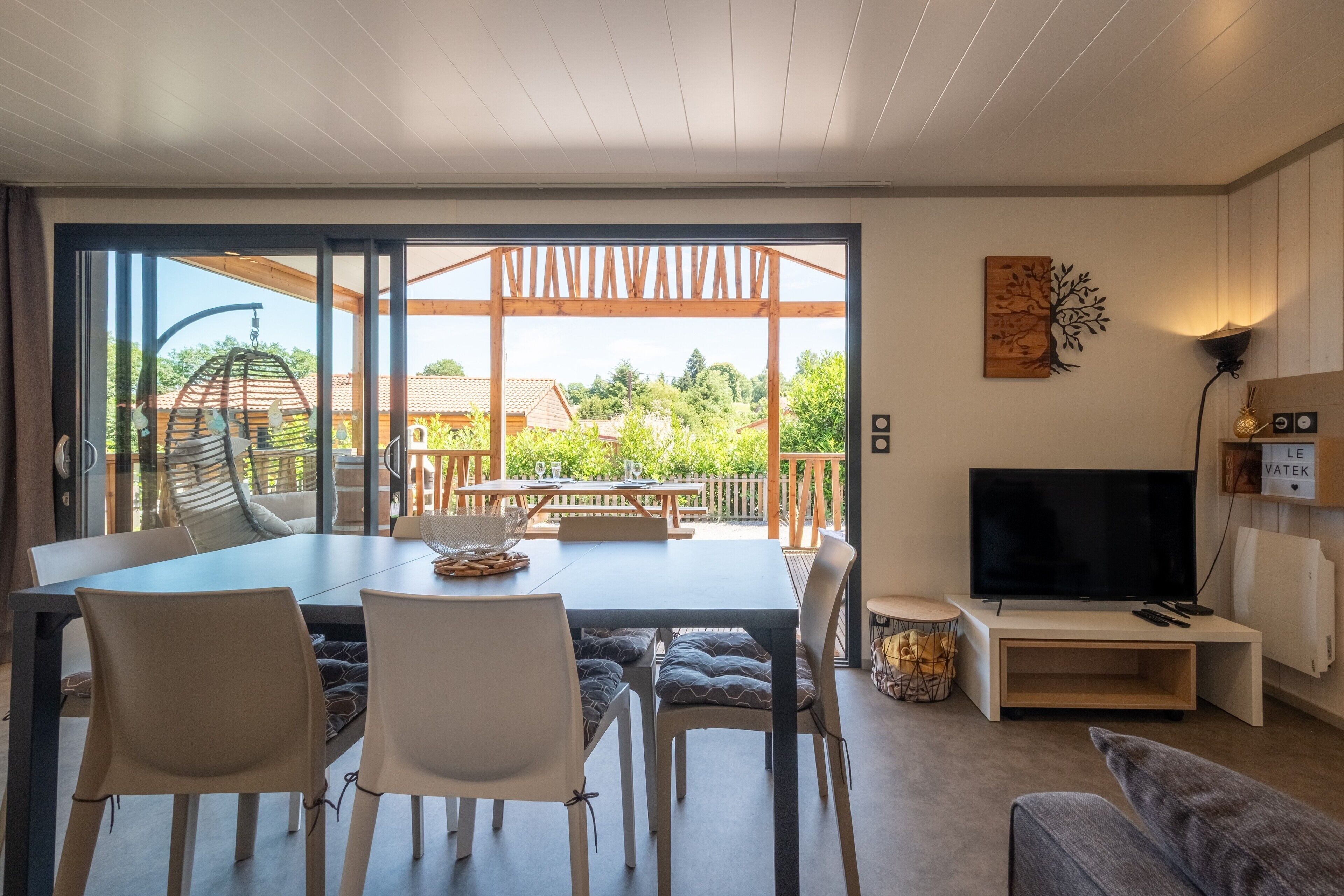 A modern living room with a dining area, a TV, and a view of the outdoors.