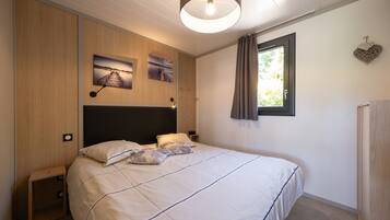 Une chambre à coucher avec un lit, un lambris en bois, une tête de lit, une lampe fixée au mur, une fenêtre avec des rideaux et une petite table de chevet.