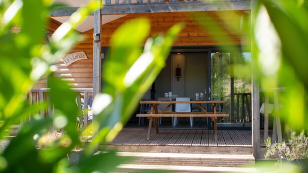Une terrasse en bois avec une table et des chaises, une enseigne indiquant « Le Vartekia », et une porte vitrée donnant sur l’intérieur.