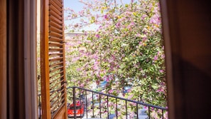 Ein Balkon mit Blick auf eine Straße, ein rotes Auto und blühende, rosa Bäume.