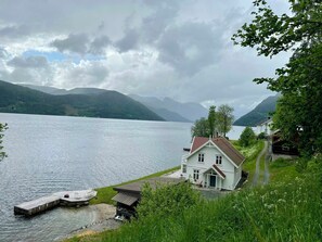 Ein Haus am Seeufer mit einer Anlegestelle, einem kleinen Boot und einem Weg zum Haus.