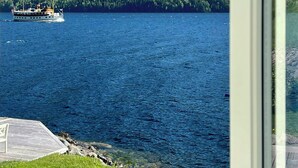 A lake with a boat, a forested hill, and a grassy area near a building. - Cabin by Telemark Canal with private beach (Høydalsmo)