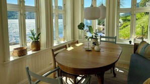 A dining area with a round table, chairs, and large windows overlooking a body of water. - Cabin by Telemark Canal with private beach (Høydalsmo)