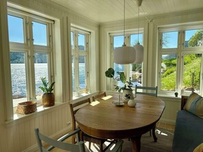 Ein Essbereich mit einem runden Tisch, Stühlen und großen Fenstern mit Blick auf ein Gewässer.