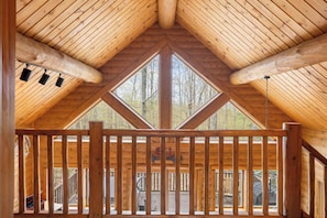 Une cabane en bois avec un toit en pente, un balcon doté de balustrades et une grande fenêtre donnant sur la forêt.