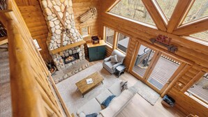 En stuga byggd av timmer med en inre inredning som inkluderar en öppen spis i sten, en soffa, ett soffbord och en skylt som visar var ett skidområde ligger.