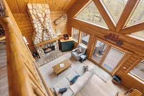 L’intérieur d’une cabane en rondins, avec une cheminée en pierre, un canapé, une table basse et un panneau indiquant une zone de ski.