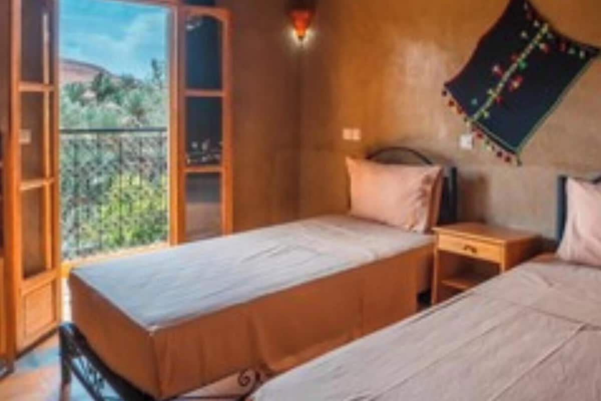A bedroom with two beds, a balcony, and a view of greenery.